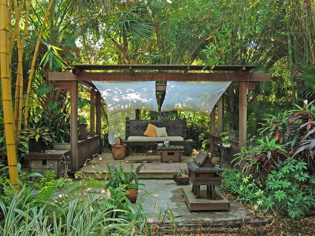 A view of a tropical garden with a seating in the middle and wooden furniture