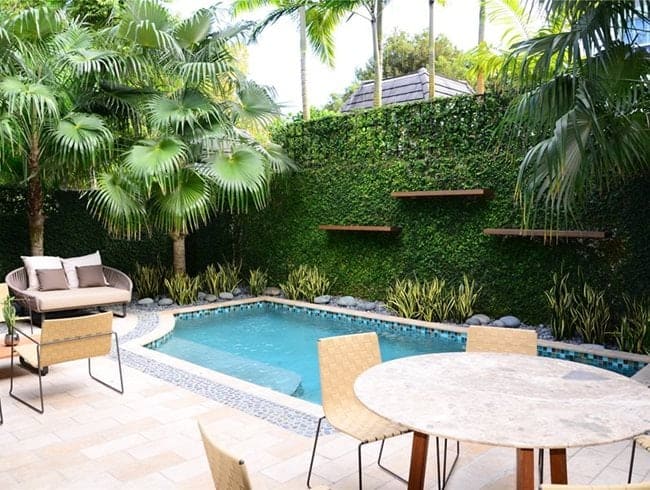 A view of plants backdrop inside a garden with pool and table and chairs